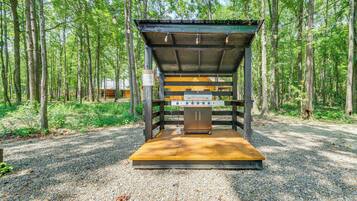 A covered outdoor grill area in a forested setting.