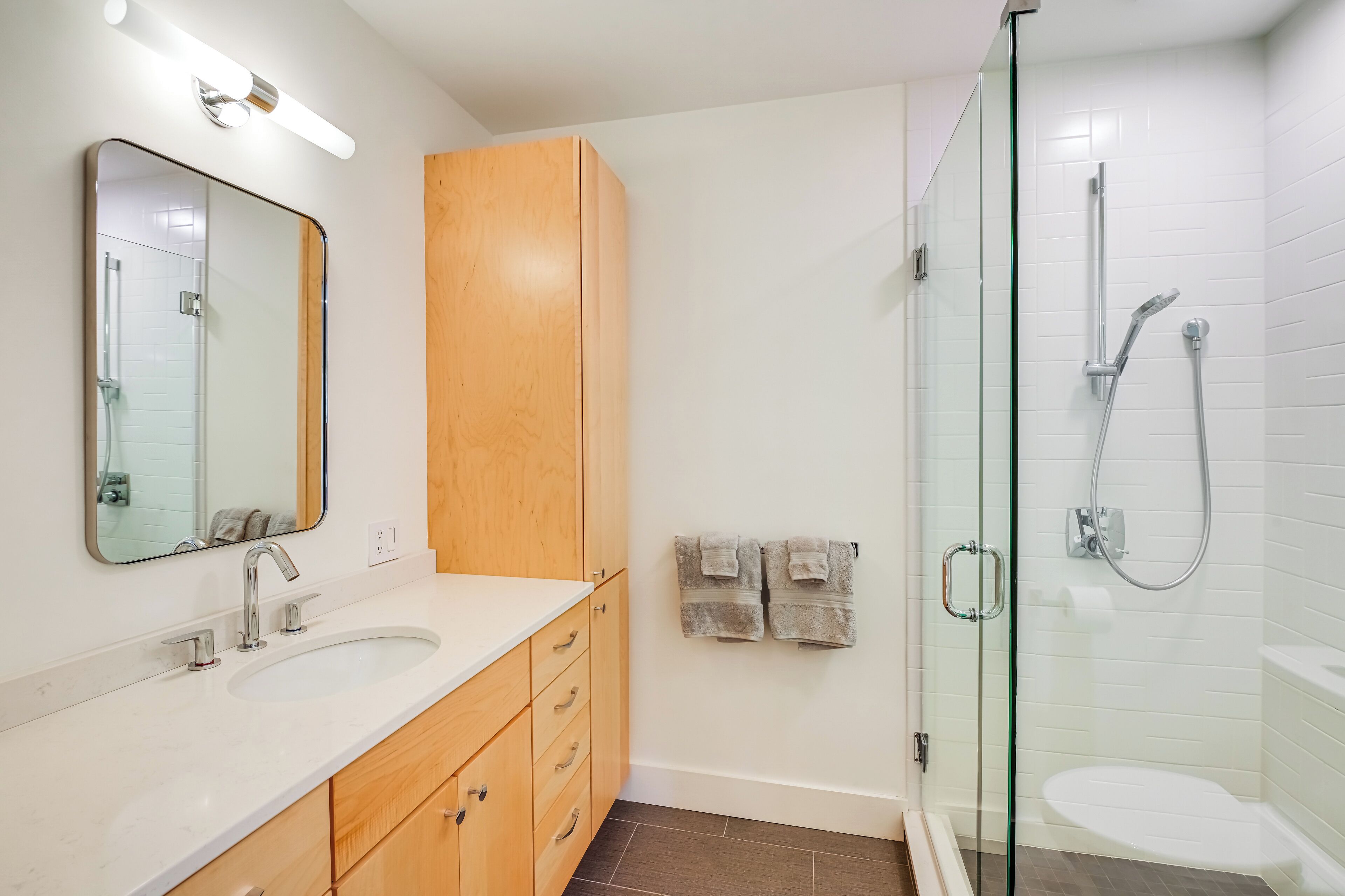Un baño moderno con cabina de ducha de vidrio, un lavamanos blanco y armarios de madera.