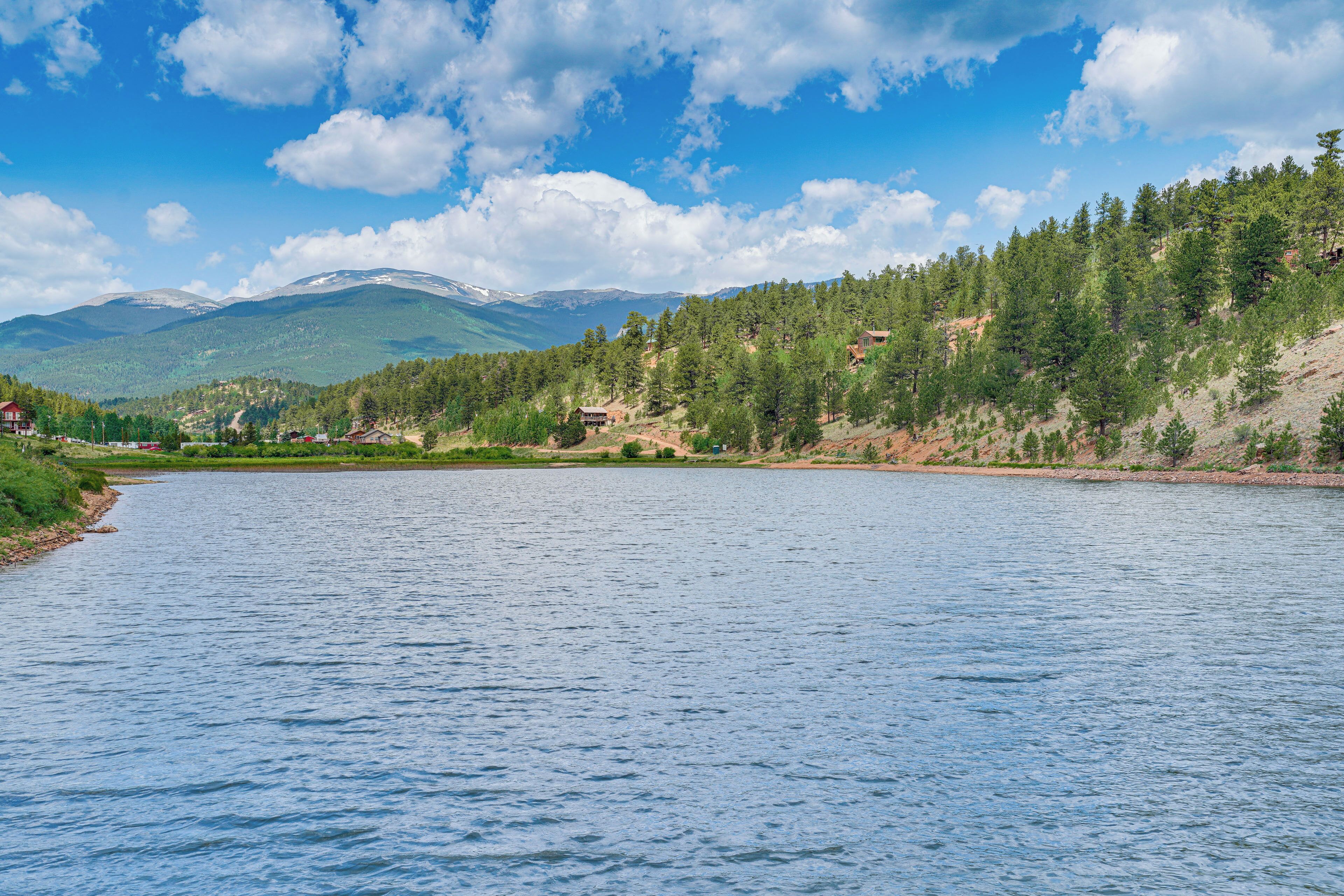 A river with a forested hillside and mountains in the background.
