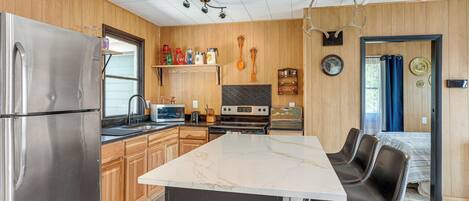A modern kitchen with wooden paneling, stainless steel appliances, a marble island, and a dining area with leather chairs.