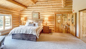 Quarto de cabana de toras com cama de madeira, luminárias de cabeceira, guarda-roupa de madeira e uma janela grande.