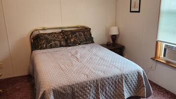Une chambre à coucher avec un lit, une table de chevet, une lampe, un tableau au mur et une fenêtre avec des stores.