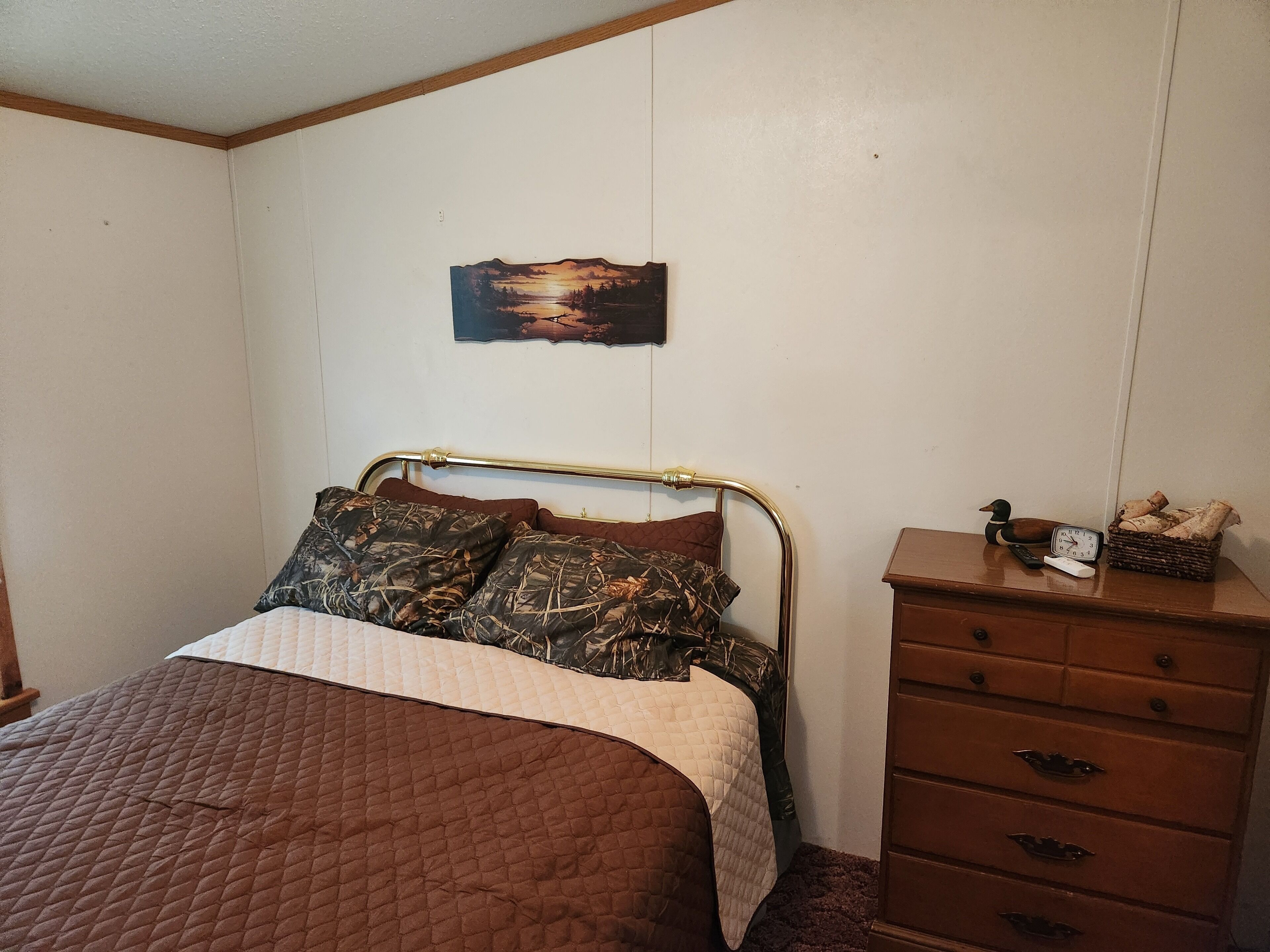 Een slaapkamer met een bed, een houten dressoir, een schilderij en een klok.