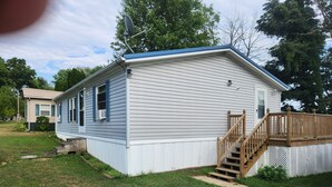 A single-story mobile home with a front deck and a small staircase leading to the entrance. - Hunters Haven a charming 3-br house in welcoming Piedmont Ohio with AC, Wi-Fi.  (Freeport)