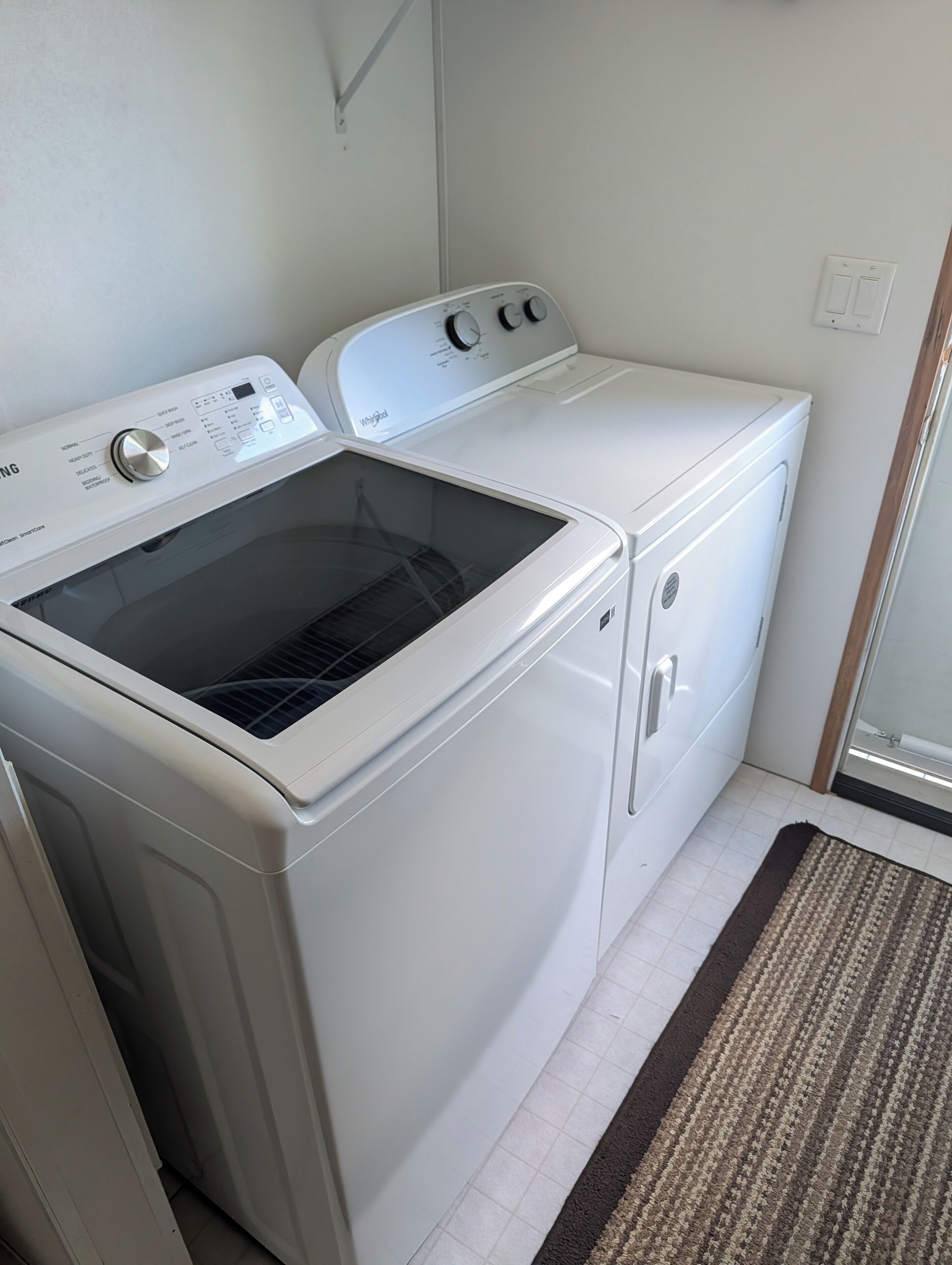 Een kleine wasruimte met een voorlader wasmachine en droger, een klein opstapje en een deur naar een andere kamer.