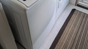 A compact laundry room with a front-loading washer and dryer, a small step, and a door leading to another room. - Hunters Haven a charming 3-br house in welcoming Piedmont Ohio with AC, Wi-Fi.  (Freeport)