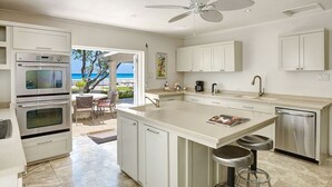 Uma cozinha moderna com armários brancos, uma ilha grande com banquetas e vista para o mar.