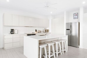 A modern kitchen with white cabinetry, a stainless steel refrigerator, and a central island with bar stools. - Westmoreland Hills - Whitehaven by Blue Sky Luxury (Holetown)