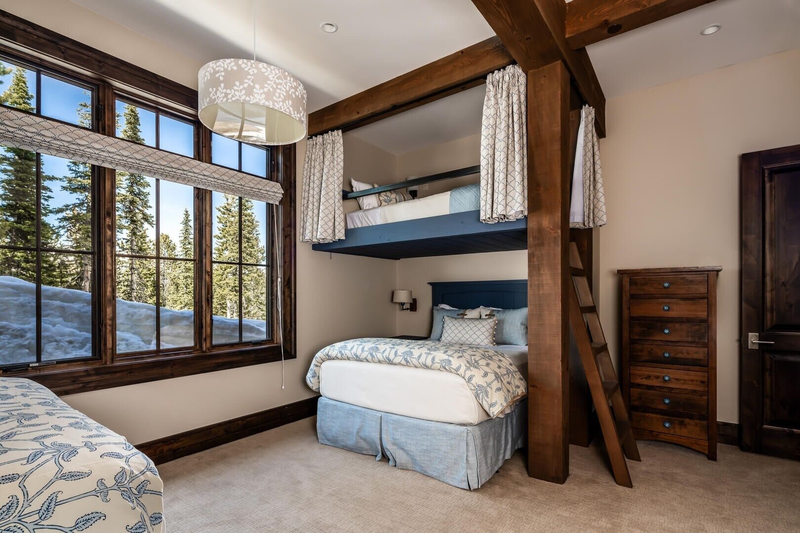 A bedroom with a bunk bed, a dresser, and a window with a view of trees and snow.