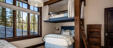 A bedroom with a bunk bed, a dresser, and a window with a view of trees and snow.