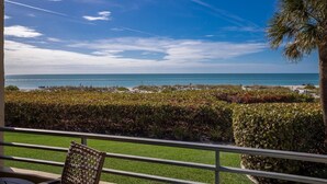 A view from a balcony overlooking a beach with a palm tree and a chair. - 4200 Gulf Drive Unit 108 2 Bedroom Home by RedAwning (Holmes Beach)