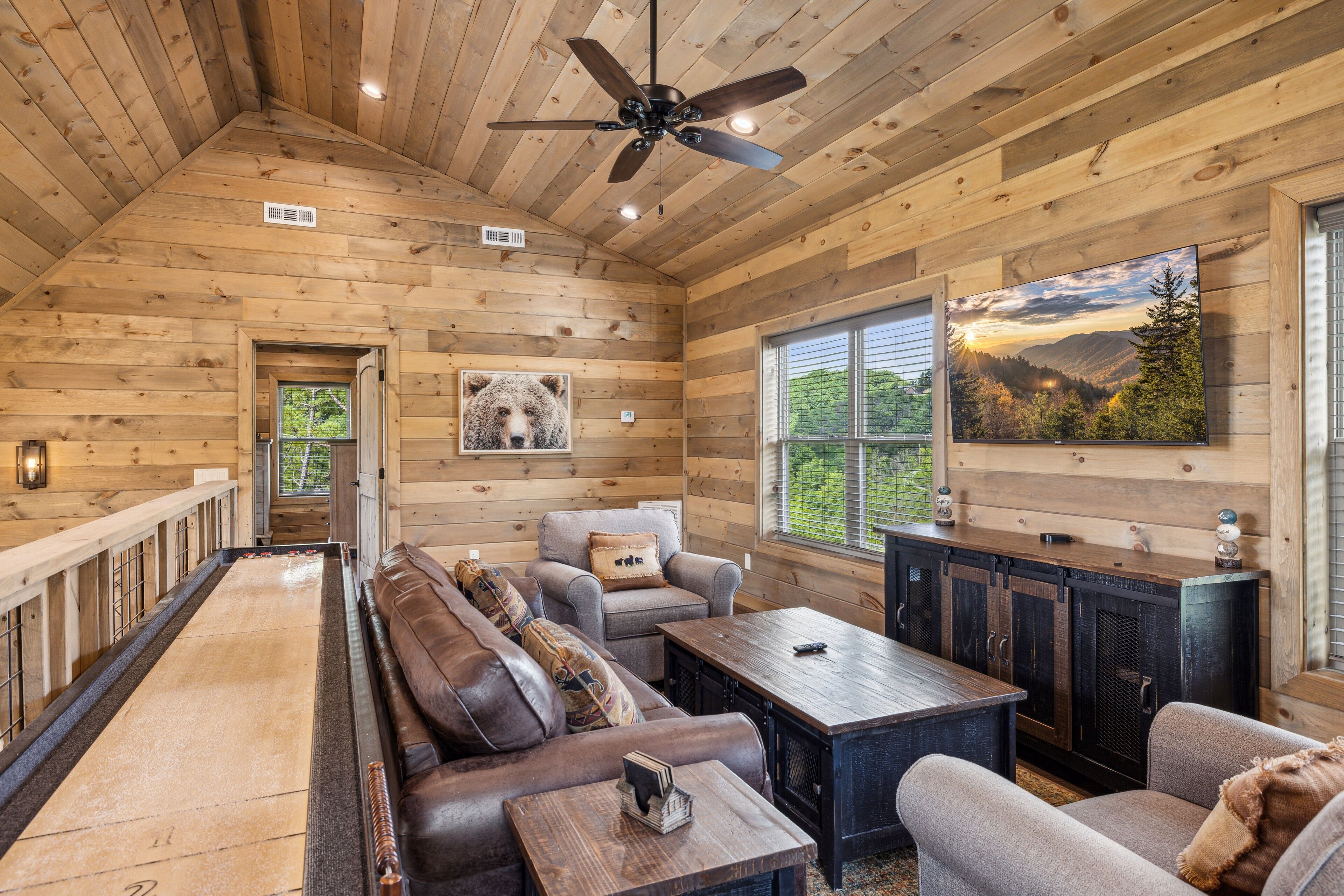 Interior acogedor de una cabaña con techo de madera, un ventanal grande, chimenea y mesa de billar.