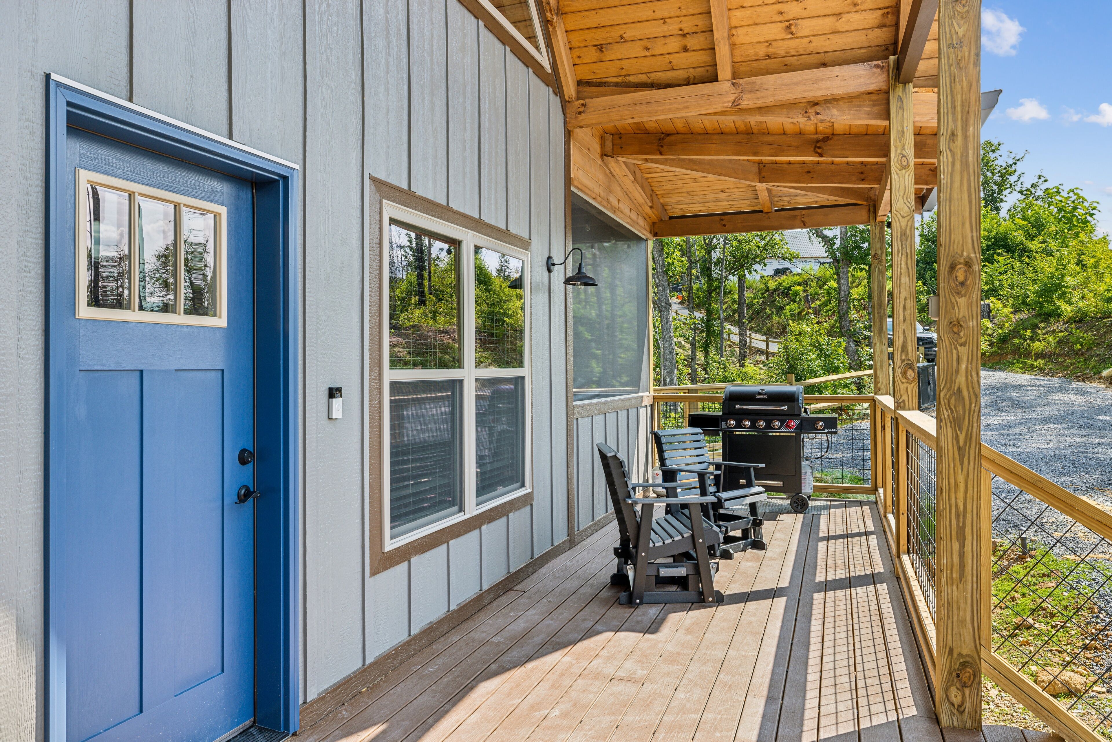 Eine Holzterrasse mit blauer Tür, Grill und Sitzgelegenheit im Freien.