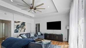 A modern living room with a ceiling fan, a flat-screen TV, and a dark wooden cabinet. - Sea View Cottage - 110 Ponce De Leon 3 Bedroom Home by RedAwning (Dauphin Island)