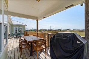 A covered outdoor deck with a wooden table and chairs, a barbecue grill, and a view of the surrounding area.