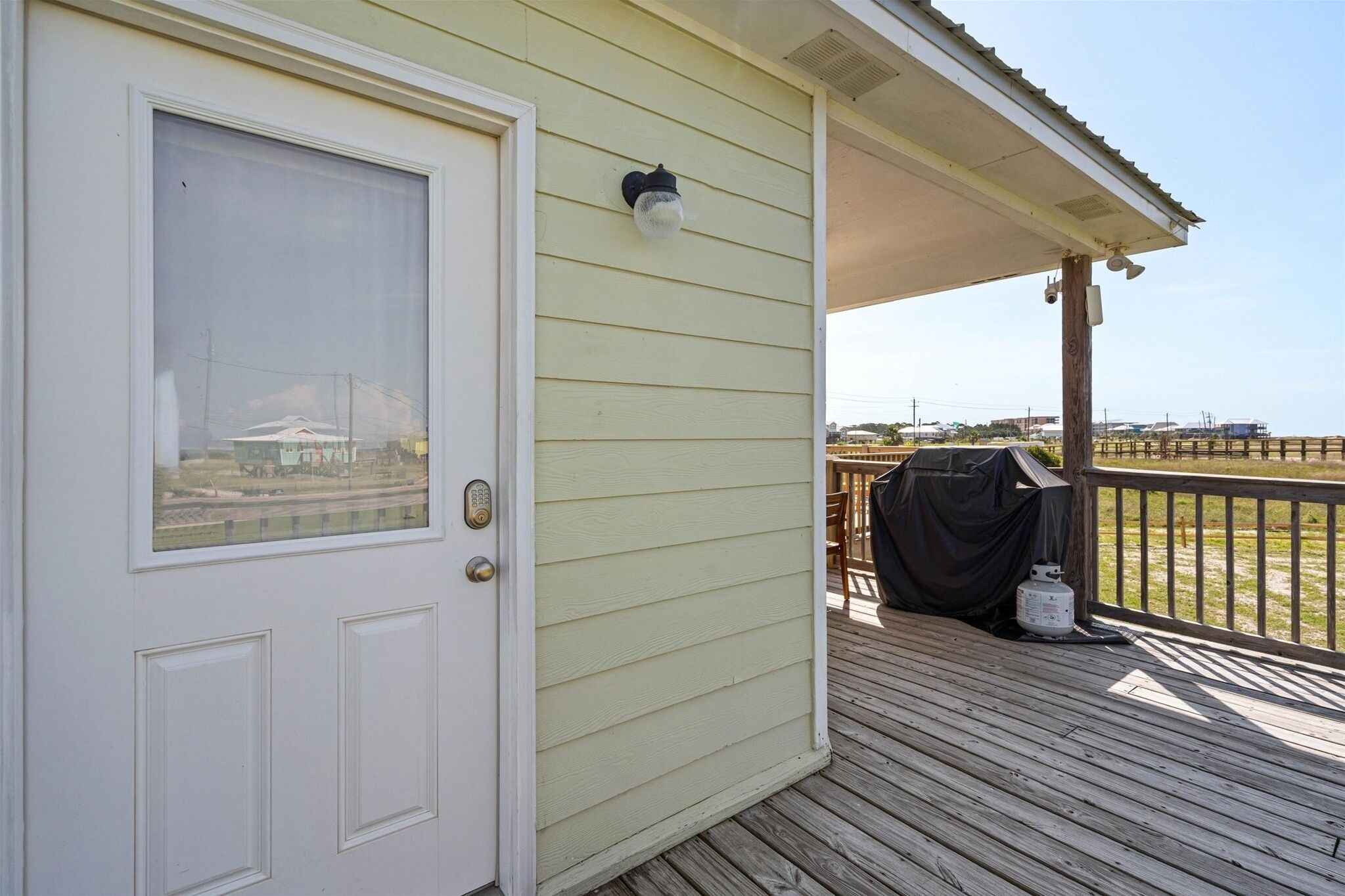 A wooden deck with a covered area, a door with a window, and a barbecue grill.
