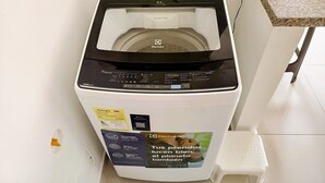 Vue de face d’un lave-linge, avec son panneau de commande, un tuyau d’arrivée d’eau et un compartiment à lessive.