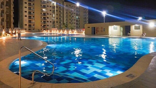 Une piscine aux motifs à carreaux bleus, entourée d’une petite clôture et éclairée par des lampes suspendues au plafond.