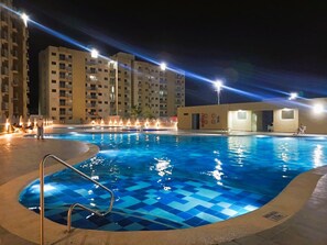 A swimming pool with a blue checkered pattern, surrounded by a low fence and illuminated by overhead lights. - Apartamento Aviva Sierra (Santa Marta)