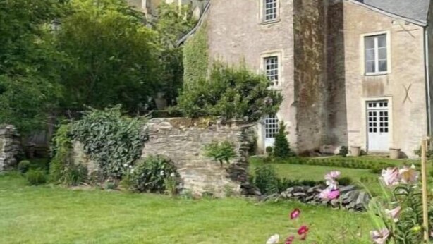 Un edificio de piedra histórico con una torre, rodeado de un jardín bien cuidado y diversas flores.