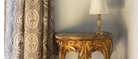 Ein Zimmer mit gemusterten Vorhängen, einem gerahmten Bild an der Wand und einem Tisch mit einer Lampe.