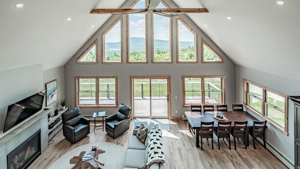 A spacious loft with a high ceiling, large windows, a fireplace, a dining area, and a cozy seating area. - The Best Mountain Views! You can't stop looking at them! (Hanover)