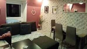 A living room with a sofa, a dining table, and chairs. There is a window with a view of the outside. - Beautiful, Quite and Modern Flat, Near the Nature and Railway Station (Karpacz)