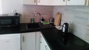 A kitchen with white cabinets, a black countertop, a microwave, a sink with a dish soap bottle, and a kettle. - Beautiful, Quite and Modern Flat, Near the Nature and Railway Station (Karpacz)