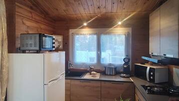 A compact kitchen with wooden walls, a refrigerator, a microwave, and a sink.