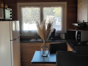 Una cocina con refrigerador, microondas, estufa y ventana con vista a árboles.