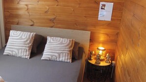 Una habitación acogedora con una cama, almohadas, una mesita de noche con lámpara y una pequeña mesa redonda con adornos.