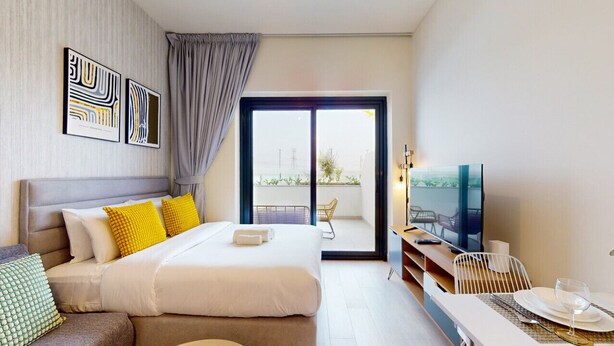 A hotel room with a bed, a TV, a dining area, and a balcony with a view.