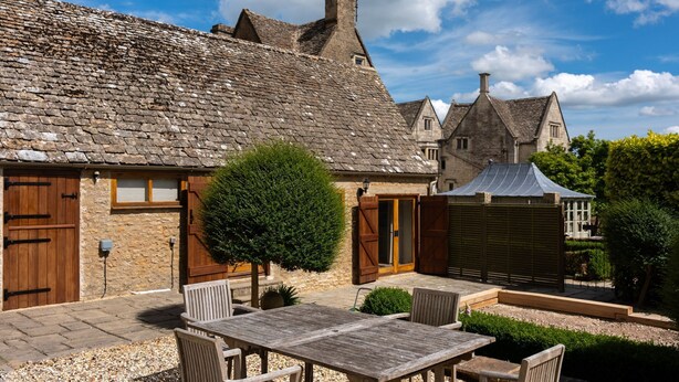 A stone building with a tiled roof, a wooden door, and a small window. There is a wooden table and chairs in the foreground. - Dog friendly, two bedroom holiday cottage in heart of Cotswolds (Painswick)