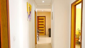 Um corredor com piso de azulejos, portas de madeira e uma área de refeições ao fundo.