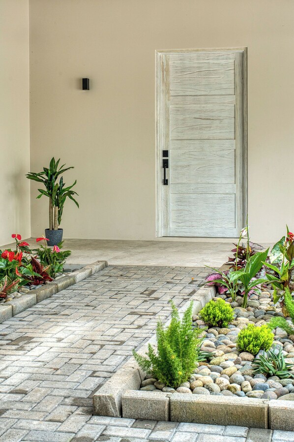 Uma entrada limpa e minimalista, com um caminho de pedras que leva a uma porta.