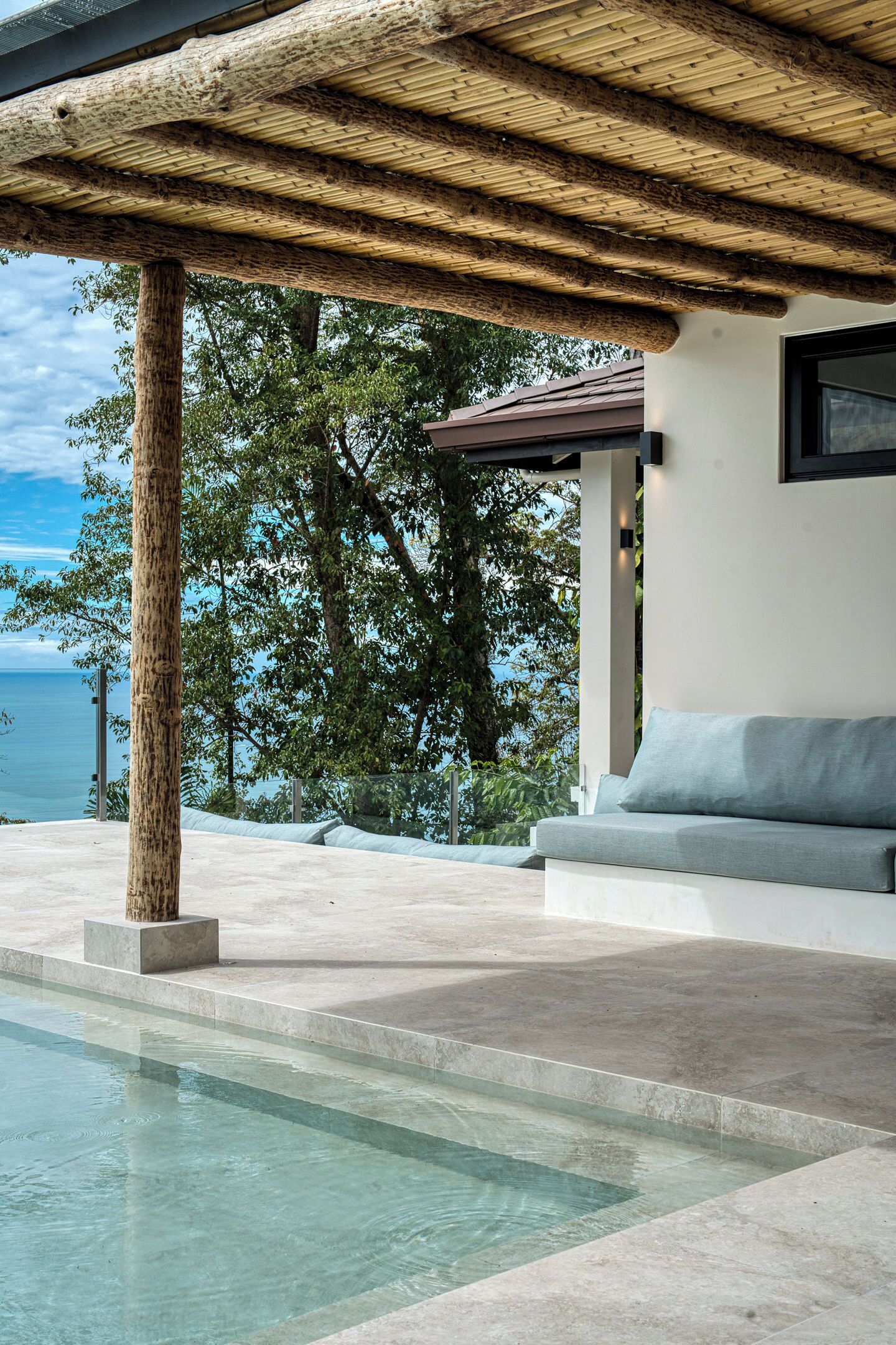 A pool area with a pergola, a seating area, and a view of the sea.