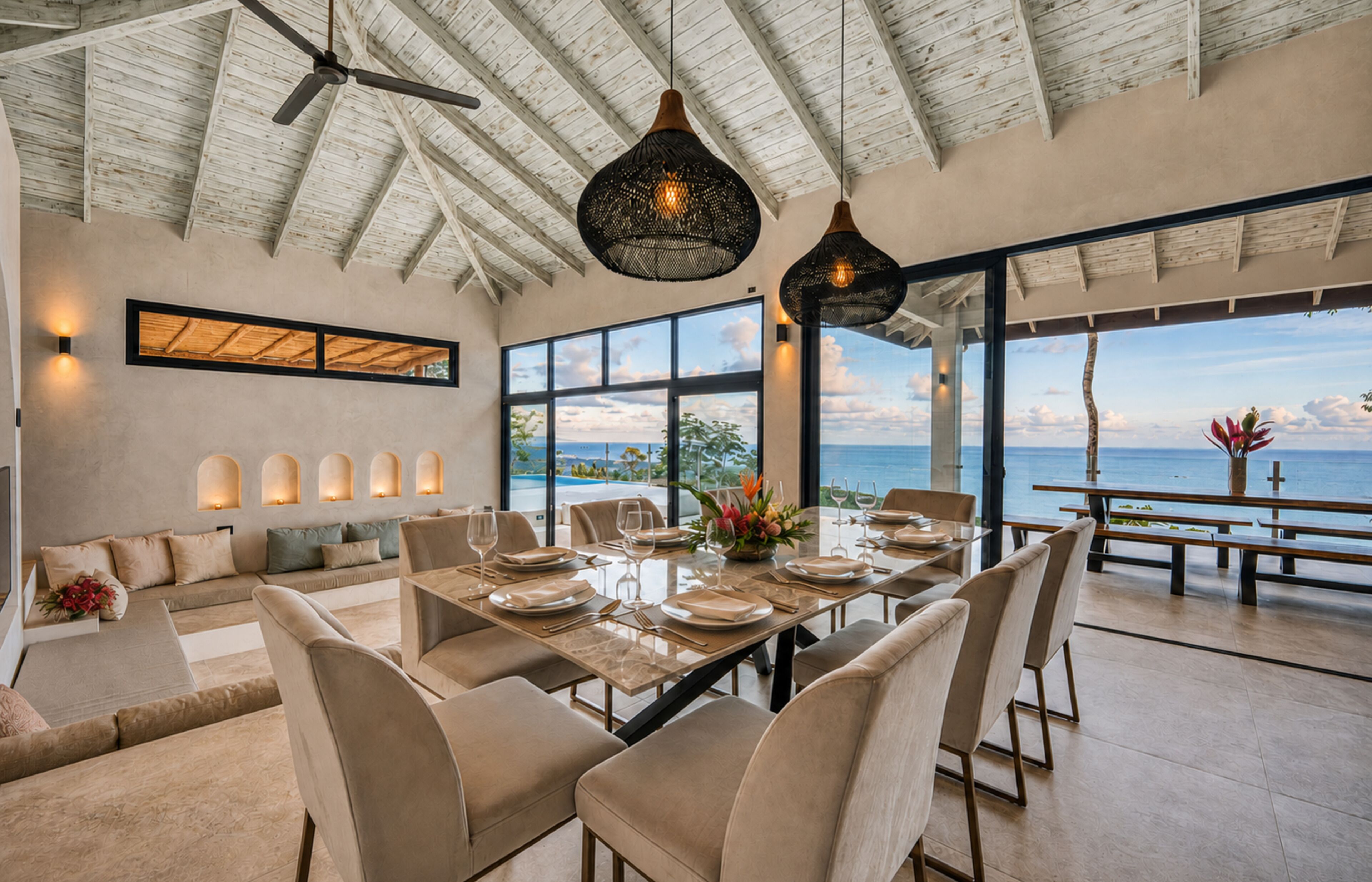 A spacious dining area with a view of the ocean, a ceiling fan, and a modern chandelier.