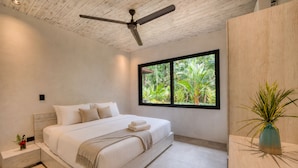 Une chambre moderne avec un grand lit, un ventilateur de plafond, une fenêtre donnant sur un paysage verdoyant et une table de chevet agrémentée d’un vase.