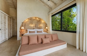 A bedroom with a bed, a sofa, a large window, and a wall with a textured pattern.