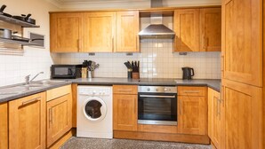 A modern kitchen with wooden cabinets, a washing machine, an oven, and a microwave.