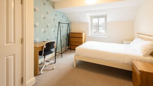 A bedroom with a bed, a desk with a chair, a wardrobe, and a window.