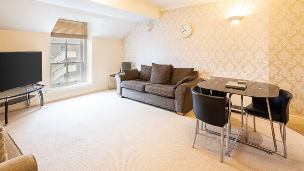 A living room with a sofa, a TV, a dining table with chairs, and a patterned wallpaper.