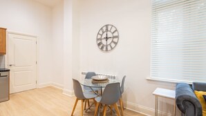 A dining area with a glass table, grey chairs, and a wall clock. - Host Stay The Cathedrals (Durham)