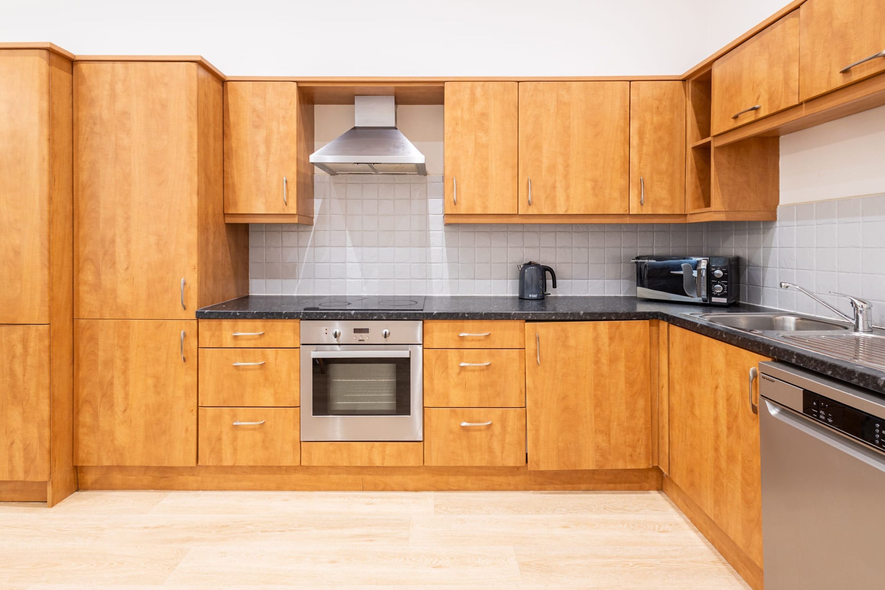 Een moderne keuken met houten kastjes, een roestvrijstalen oven, een magnetron en een vaatwasser.