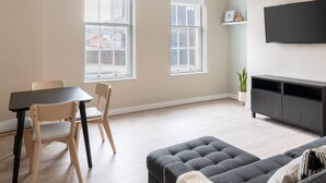 A modern living room with a grey sofa, a dining table with two chairs, and a TV mounted on the wall. - Host Stay The Quarter (Liverpool)