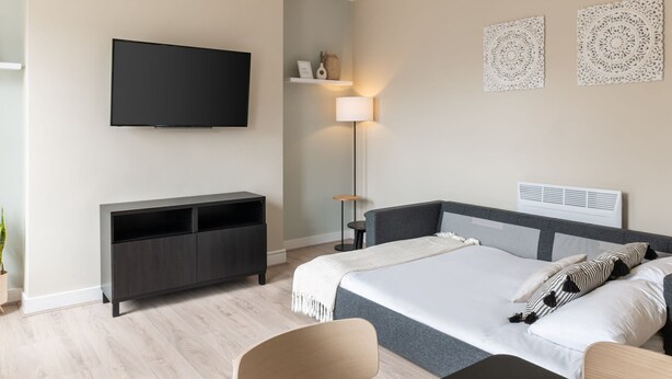A modern bedroom with a bed, bedside table, TV, and a desk. - Host Stay The Quarter (Liverpool)