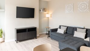 A modern living room with a grey sofa, a flat-screen TV, a floor lamp, and decorative wall art. - Host Stay The Quarter (Liverpool)