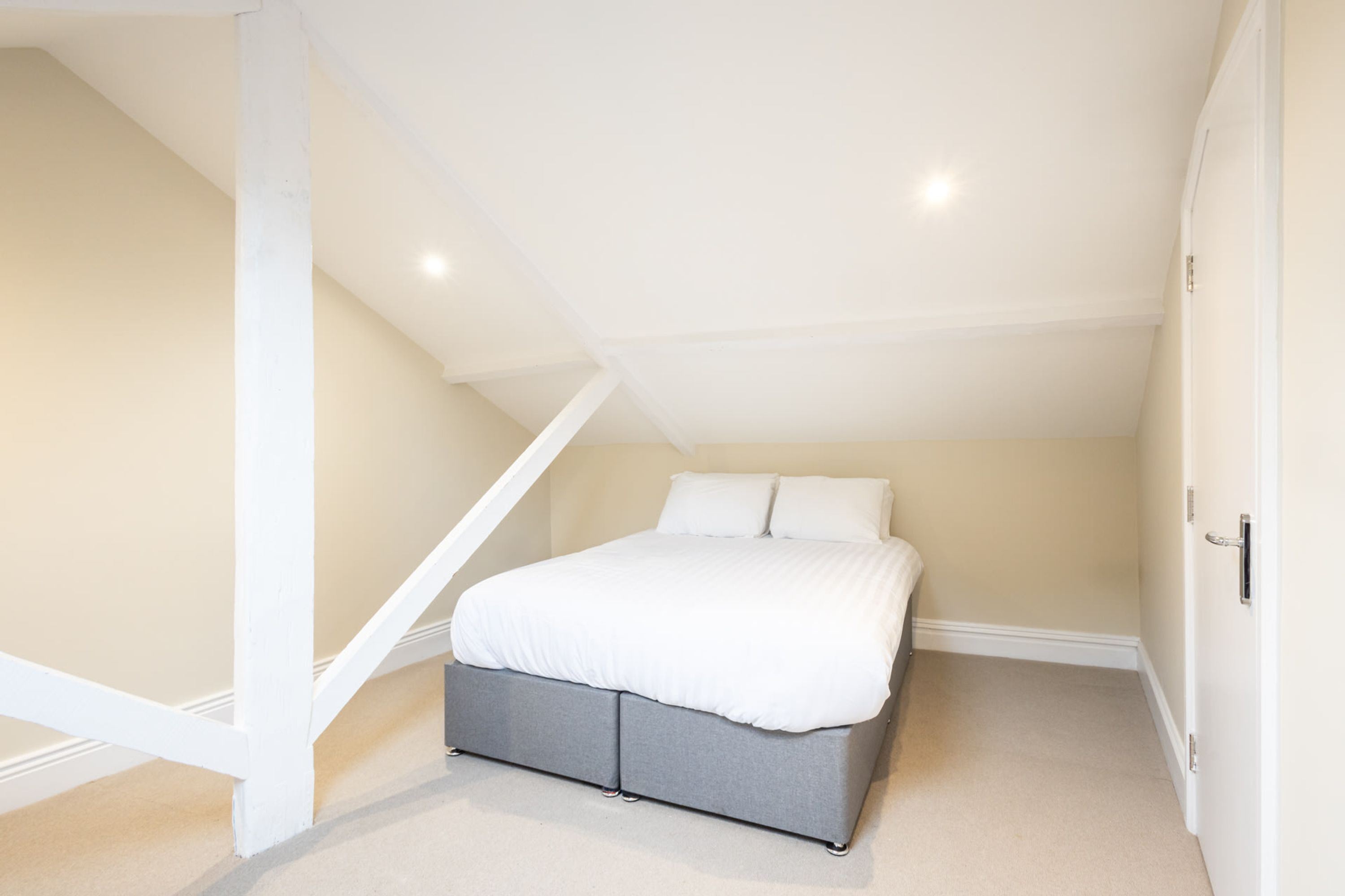 A bedroom with a bed, a white ceiling, and a sloped ceiling.