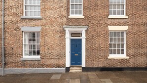 A brick building with a central blue door, white-framed windows, and a small porch area. - Host Stay Hallgarth Street (Durham)