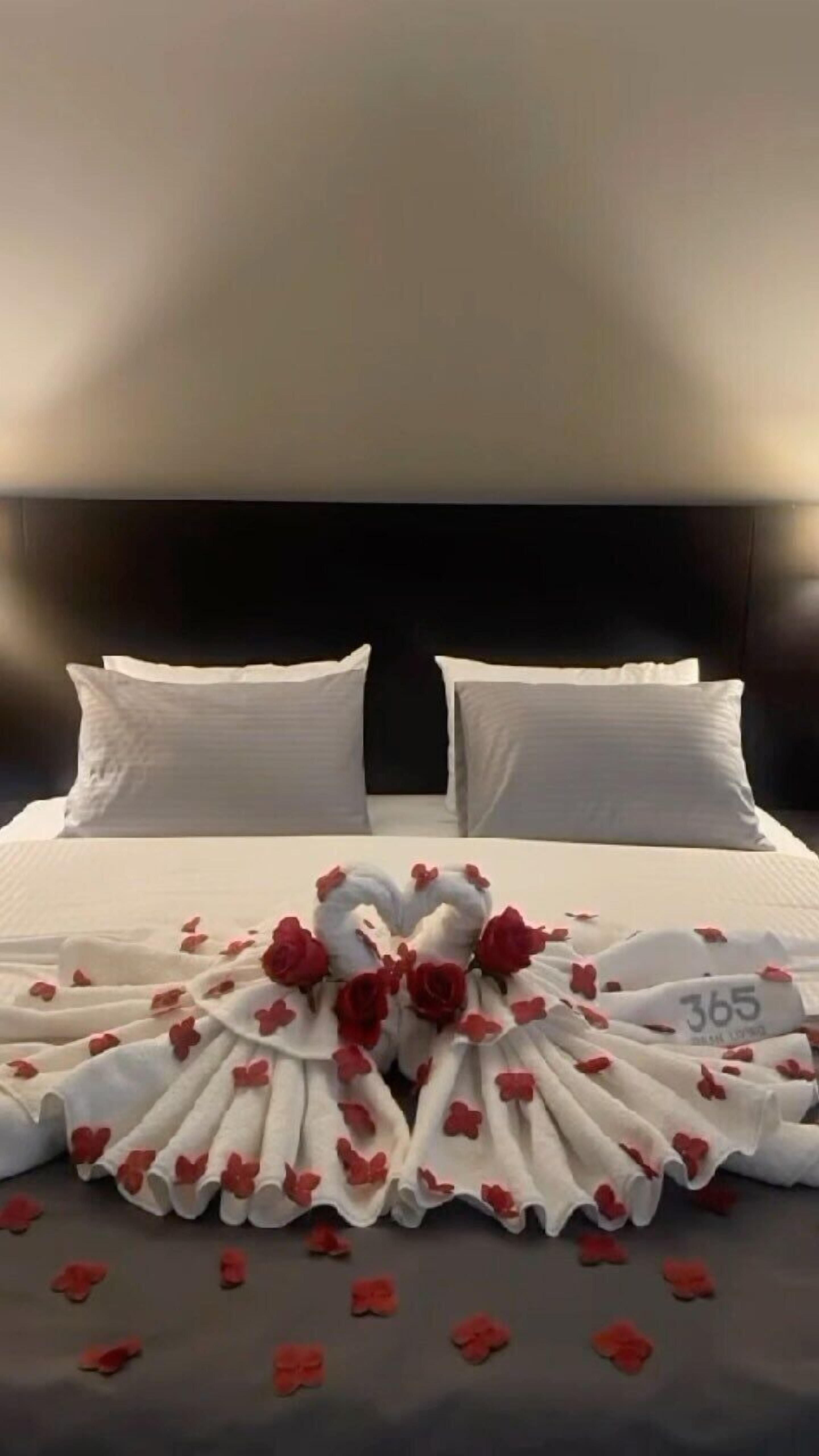 A neatly made bed with white linens and a decorative arrangement of roses and flowers.